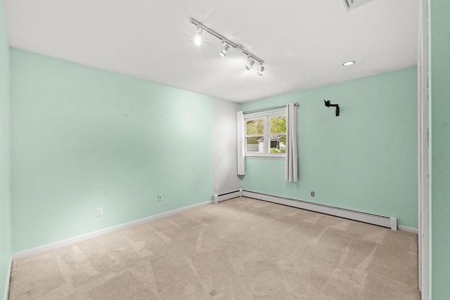 empty room featuring baseboard heating, carpet floors, track lighting, and baseboards