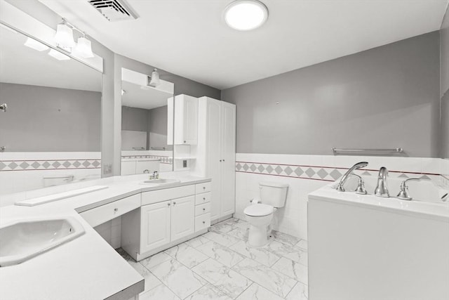 bathroom with tile walls, a wainscoted wall, marble finish floors, toilet, and double vanity