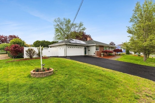 single story home with an attached garage, roof mounted solar panels, driveway, brick siding, and a chimney