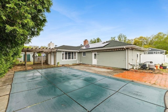 rear view of house featuring solar panels, a pergola, a patio, and a chimney