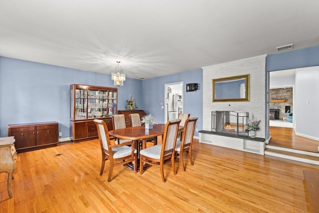 dining area featuring a multi sided fireplace, light wood-type flooring, a chandelier, and a baseboard heating unit