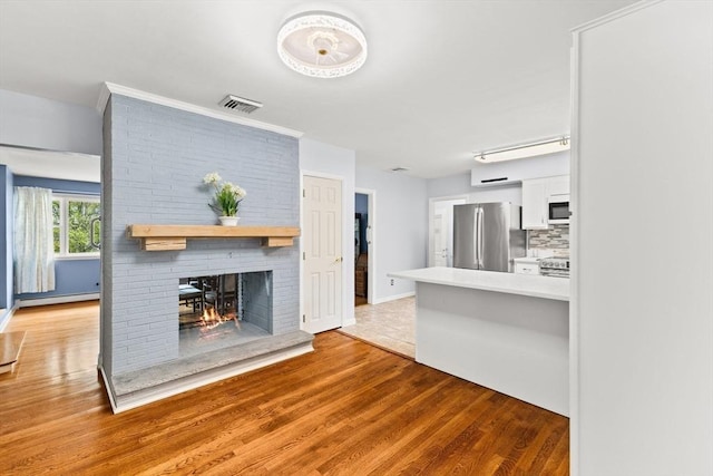 unfurnished living room with light wood finished floors, baseboard heating, a brick fireplace, and baseboards