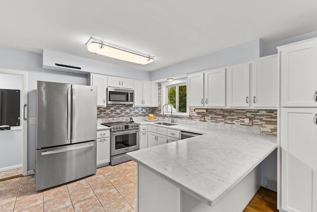 kitchen featuring appliances with stainless steel finishes, a sink, a peninsula, light countertops, and white cabinets