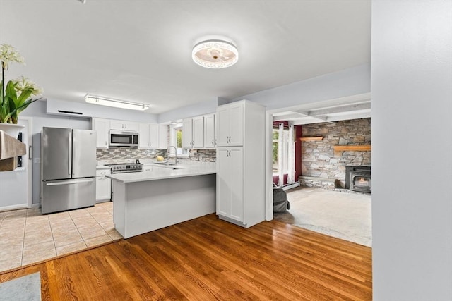 kitchen with stainless steel appliances, a sink, a peninsula, light wood-style floors, and light countertops