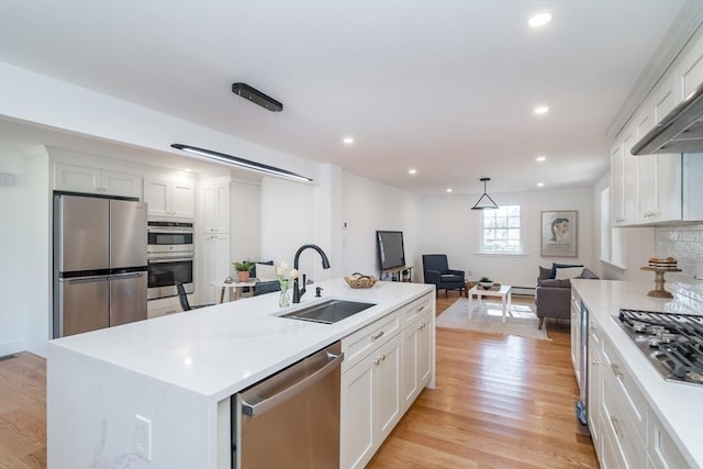 kitchen featuring light wood-type flooring, open floor plan, appliances with stainless steel finishes, and a sink