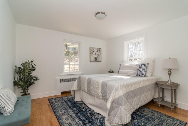 bedroom with baseboards, radiator heating unit, and light wood-style floors