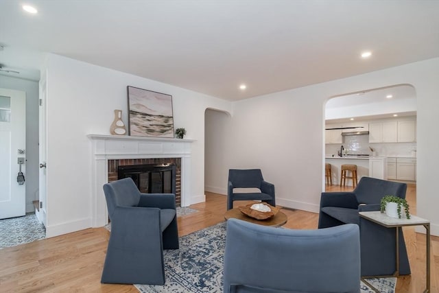 living area featuring recessed lighting, baseboards, a brick fireplace, and light wood finished floors