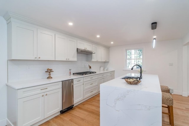 kitchen featuring light wood-type flooring, a sink, under cabinet range hood, white cabinetry, and decorative backsplash