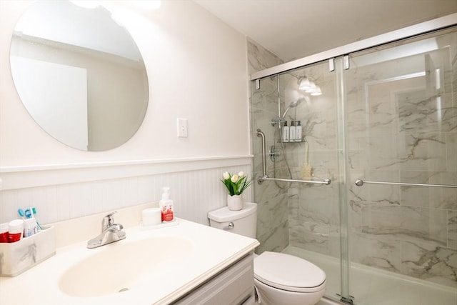 bathroom featuring a marble finish shower, toilet, a wainscoted wall, and vanity