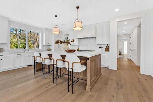 6 Willow Cir, Mashpee, MA 02649 - kitchen with light countertops, a kitchen island, white cabinetry, premium range hood, and light wood finished floors