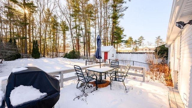 snow covered patio featuring grilling area and a storage unit