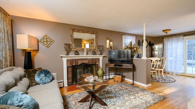 living room with a brick fireplace, baseboard heating, and light wood-type flooring