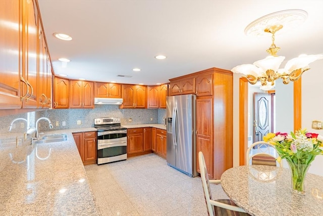 kitchen featuring under cabinet range hood, light stone counters, a sink, a notable chandelier, and stainless steel appliances