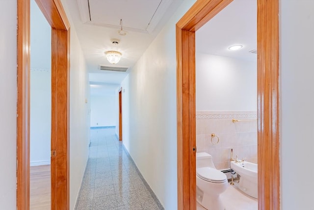 hallway with attic access, visible vents, baseboard heating, granite finish floor, and baseboards