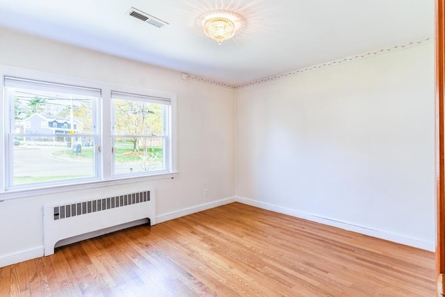 spare room with baseboards, visible vents, radiator heating unit, and light wood-style flooring
