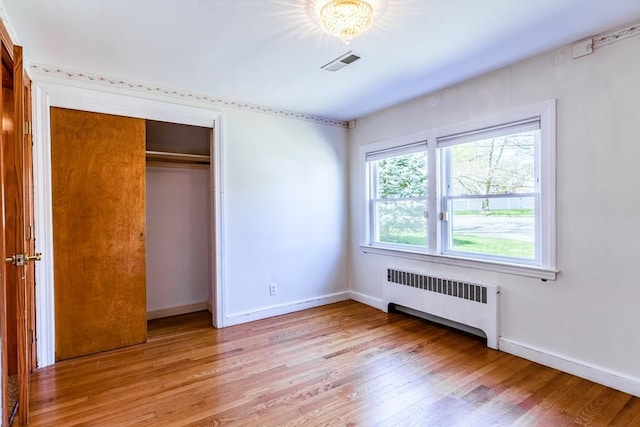 unfurnished bedroom featuring visible vents, radiator, baseboards, and light wood-type flooring