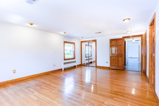 spare room featuring light wood-style floors, radiator, baseboards, and visible vents