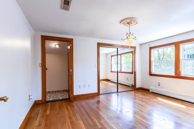unfurnished bedroom with baseboards, a baseboard radiator, wood finished floors, and a notable chandelier