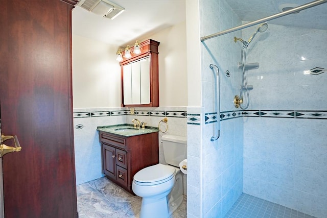 full bathroom with vanity, a tile shower, toilet, and tile walls