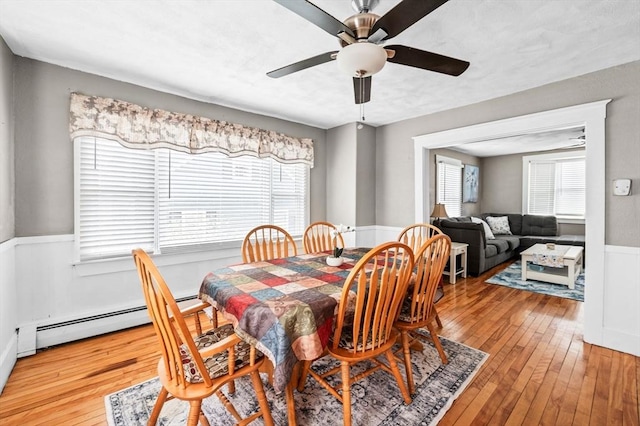 dining room with wainscoting, ceiling fan, light wood-type flooring, and baseboard heating