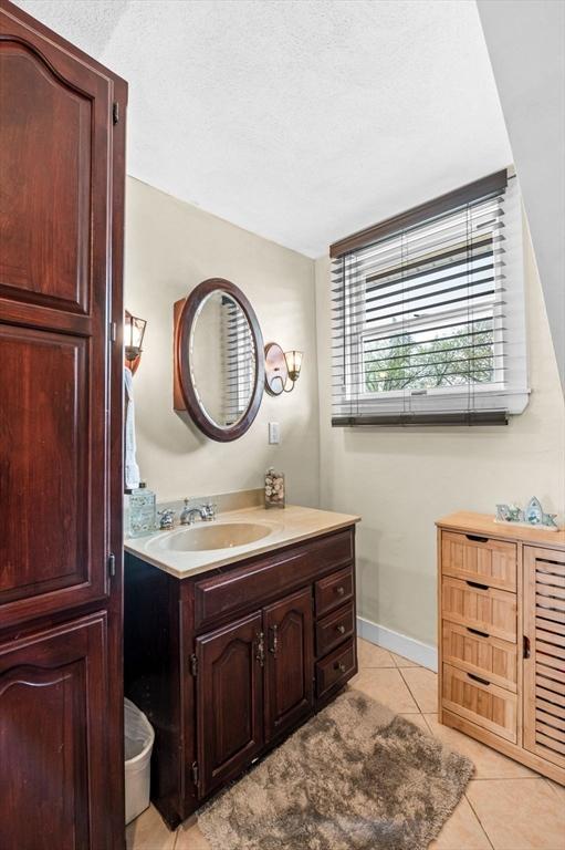 bathroom with a textured ceiling, baseboards, tile patterned flooring, and vanity