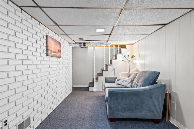 sitting room featuring a drop ceiling, carpet floors, brick wall, stairway, and visible vents