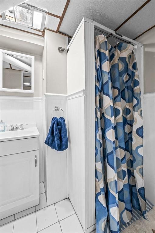 bathroom featuring a textured ceiling, wainscoting, curtained shower, tile patterned floors, and vanity