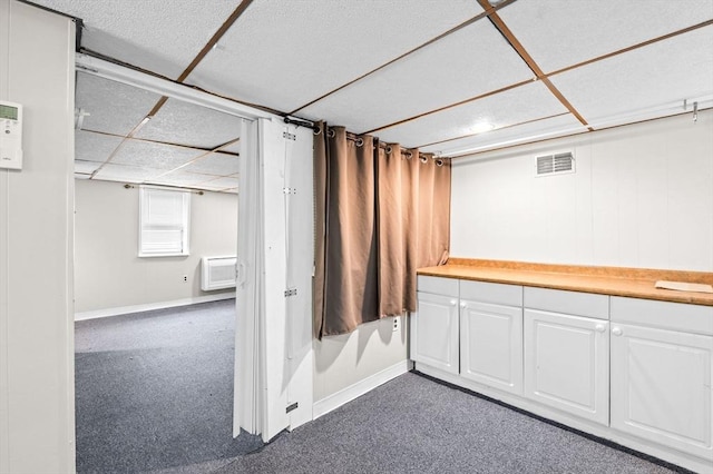 below grade area featuring baseboards, a drop ceiling, dark colored carpet, and visible vents