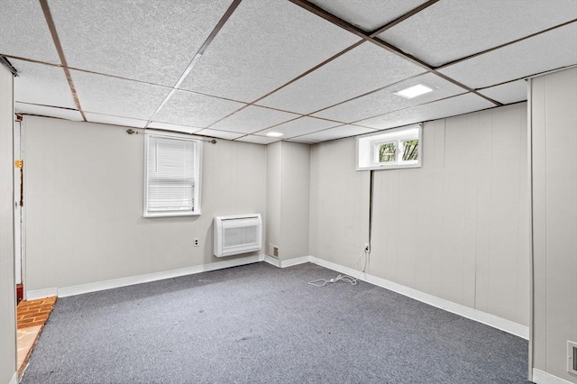 below grade area with baseboards, a drop ceiling, and heating unit