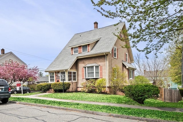 view of front of house featuring a chimney, a front yard, a shingled roof, and fence