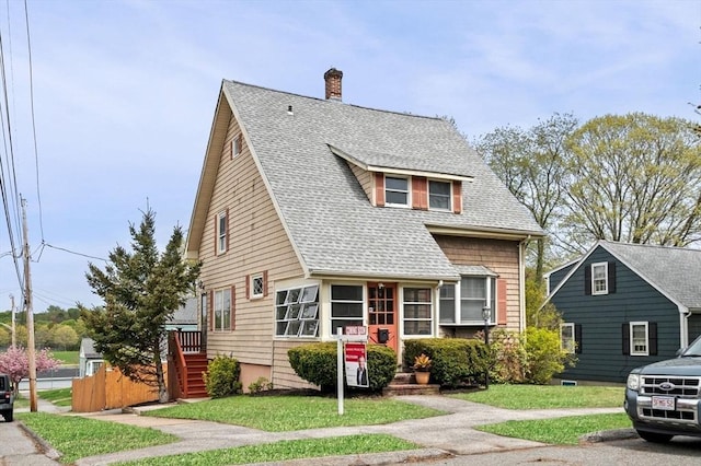 view of front of house with a front lawn, roof with shingles, and a chimney
