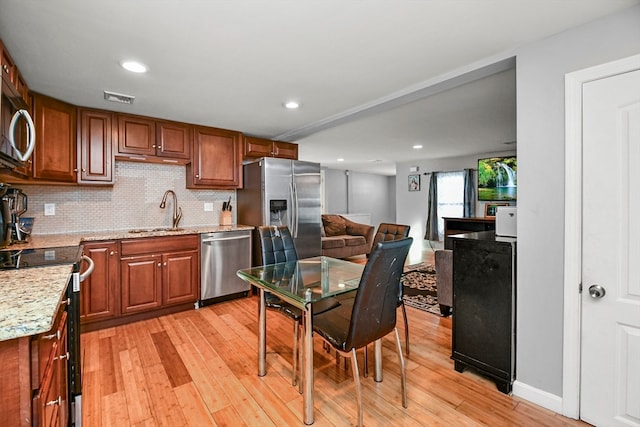 kitchen featuring tasteful backsplash, light wood-type flooring, light stone counters, stainless steel appliances, and sink