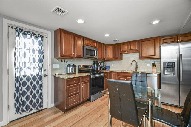 kitchen with decorative backsplash, light stone countertops, light hardwood / wood-style flooring, and stainless steel appliances