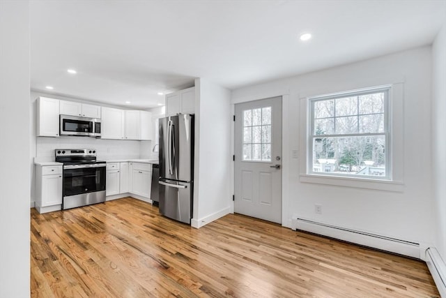 kitchen with stainless steel appliances, light hardwood / wood-style flooring, baseboard heating, white cabinets, and decorative backsplash