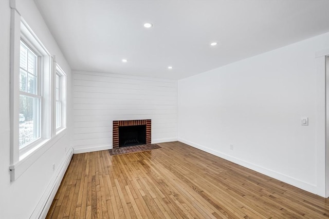 unfurnished living room featuring a brick fireplace, light hardwood / wood-style floors, a wealth of natural light, and a baseboard heating unit