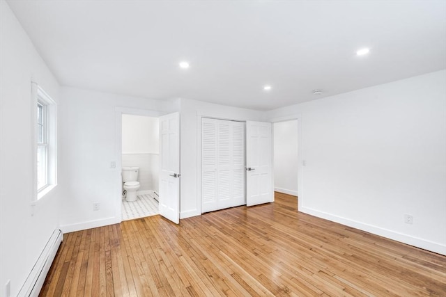 unfurnished bedroom featuring ensuite bathroom, baseboard heating, a closet, and light hardwood / wood-style flooring