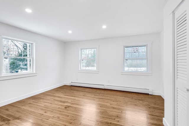 unfurnished bedroom with a baseboard heating unit, a closet, multiple windows, and light hardwood / wood-style flooring