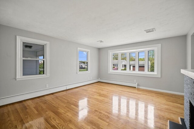 73 Mckinley Ave, Ludlow, MA 01056 - unfurnished living room featuring a fireplace with flush hearth, baseboard heating, wood finished floors, and a wealth of natural light