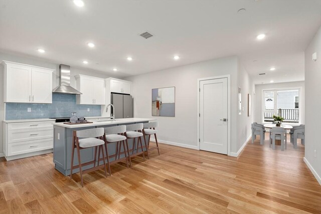 267 Old Colony Unit 205, Boston, MA 02127 - kitchen with white cabinetry, freestanding refrigerator, a kitchen island with sink, visible vents, and wall chimney exhaust hood