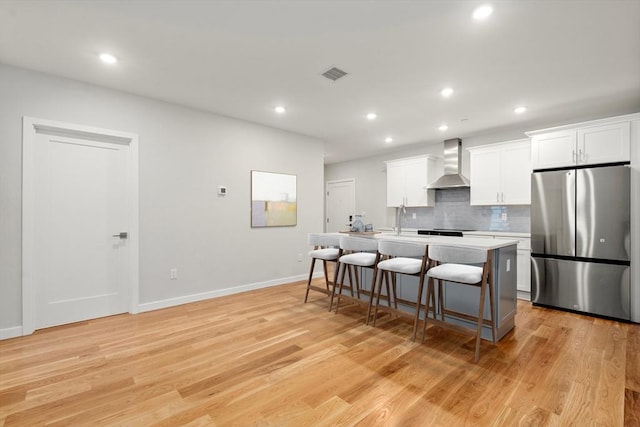 267 Old Colony Unit 205, Boston, MA 02127 - kitchen featuring visible vents, wall chimney exhaust hood, freestanding refrigerator, a center island with sink, and decorative backsplash