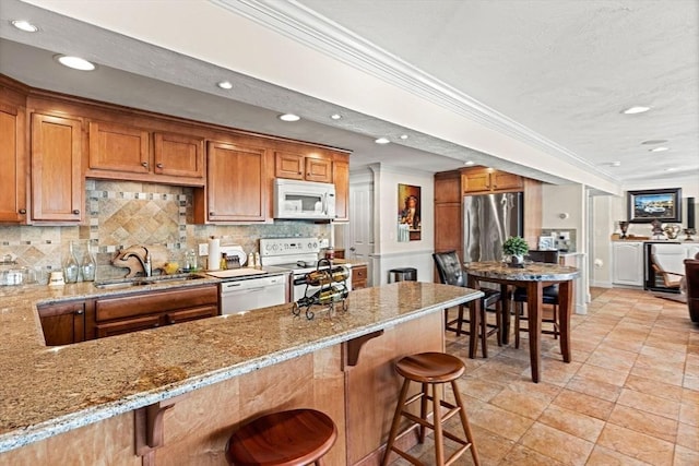 kitchen with a kitchen bar, sink, light stone counters, tasteful backsplash, and white appliances