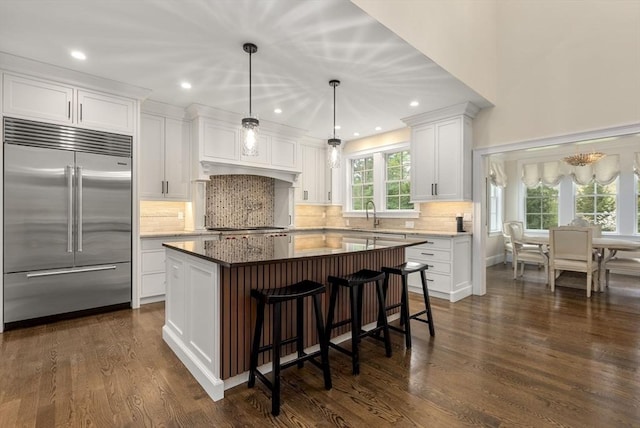 kitchen featuring decorative light fixtures, white cabinetry, stainless steel built in refrigerator, dark stone counters, and a center island