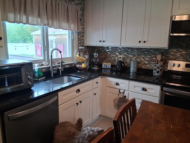 kitchen featuring appliances with stainless steel finishes, a sink, white cabinetry, tasteful backsplash, and dark stone countertops