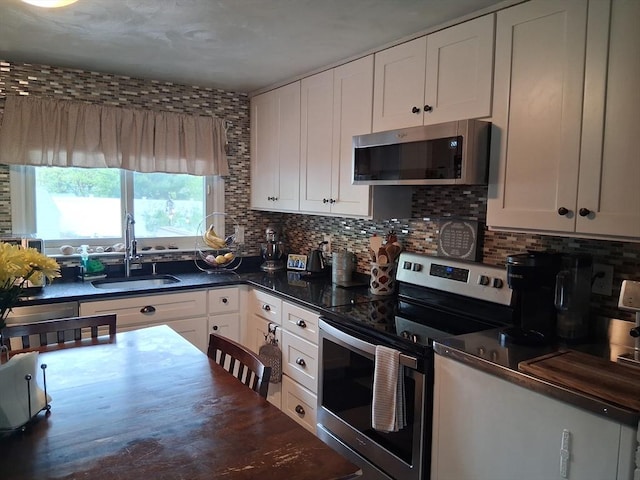 kitchen featuring stainless steel appliances, dark countertops, decorative backsplash, white cabinets, and a sink