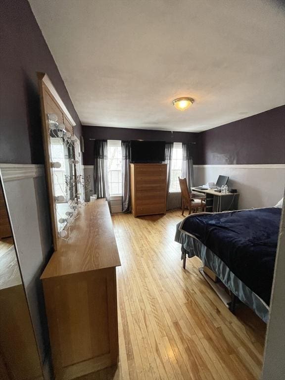 bedroom featuring a wainscoted wall, radiator heating unit, multiple windows, and light wood-type flooring