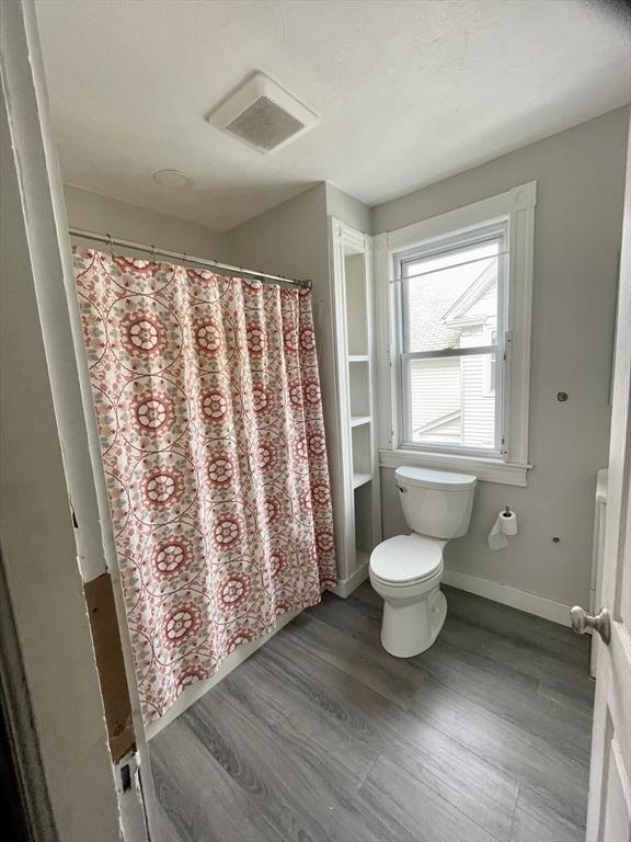 bathroom with baseboards, visible vents, a shower with shower curtain, toilet, and wood finished floors