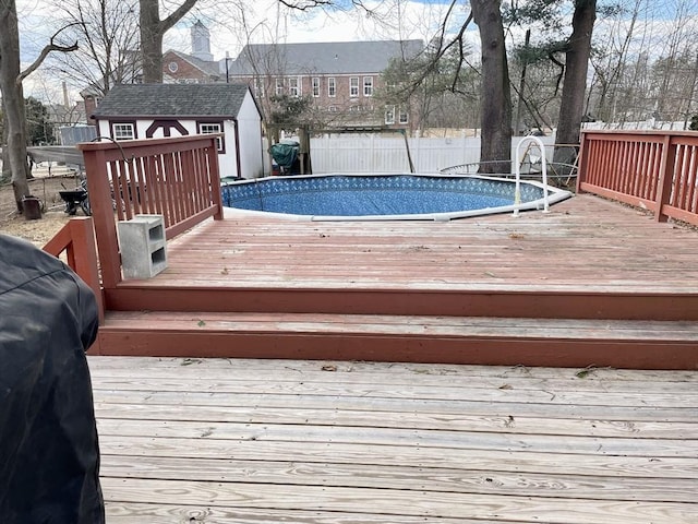 wooden terrace with a fenced in pool, an outdoor structure, fence, and a storage unit