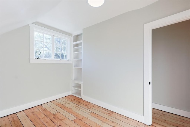 interior space featuring built in shelves, light wood-type flooring, and vaulted ceiling