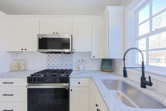 kitchen with a wealth of natural light, sink, stainless steel appliances, backsplash, and white cabinets