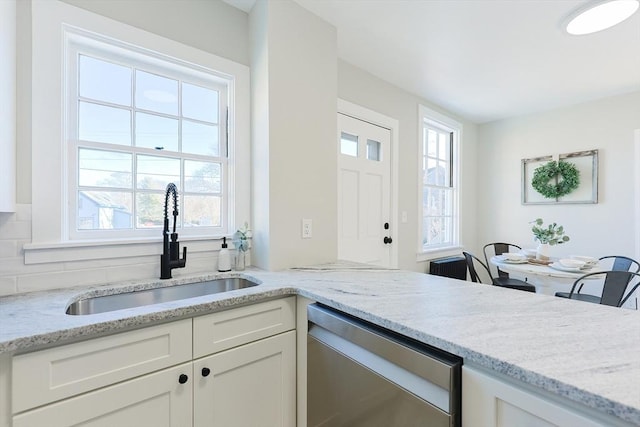 kitchen featuring backsplash, white cabinets, sink, stainless steel dishwasher, and light stone countertops